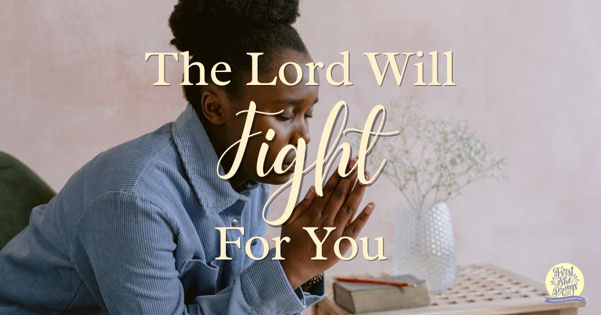 African American woman in a blue shirt praying beside an open Bible, reflecting the promise that the Lord will fight for you.